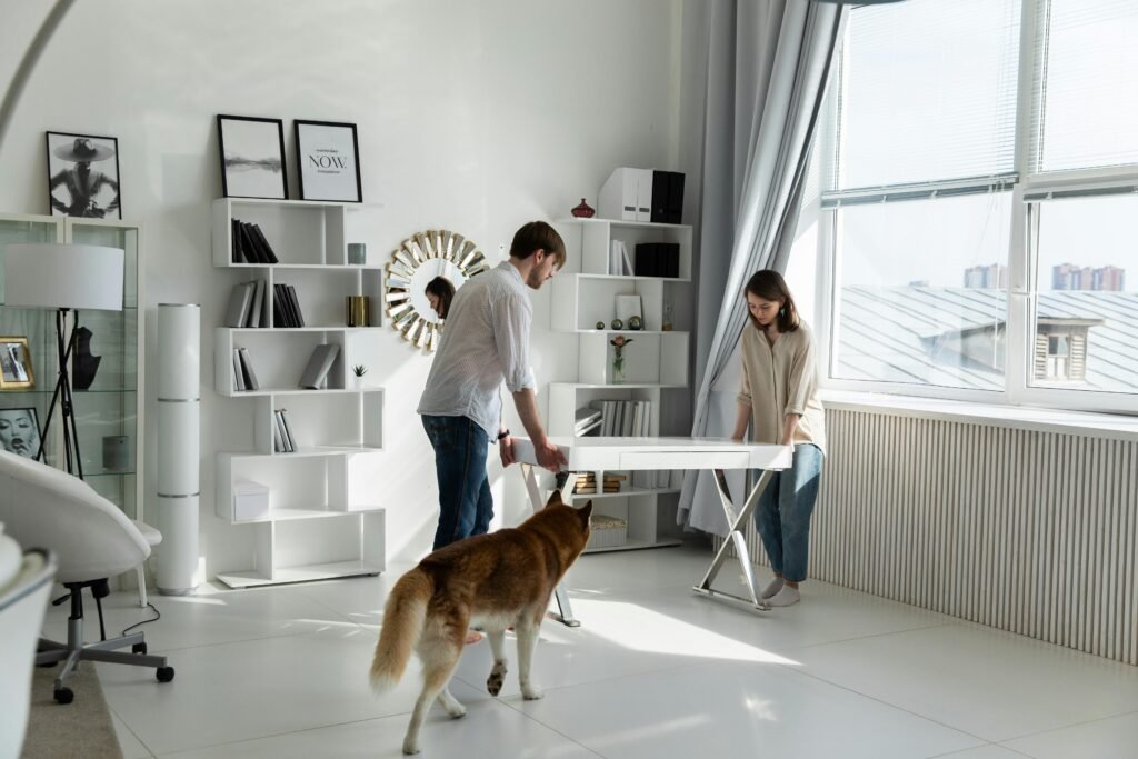 A couple arranging a white desk in a bright, modern home office with a dog present, pet friendly.